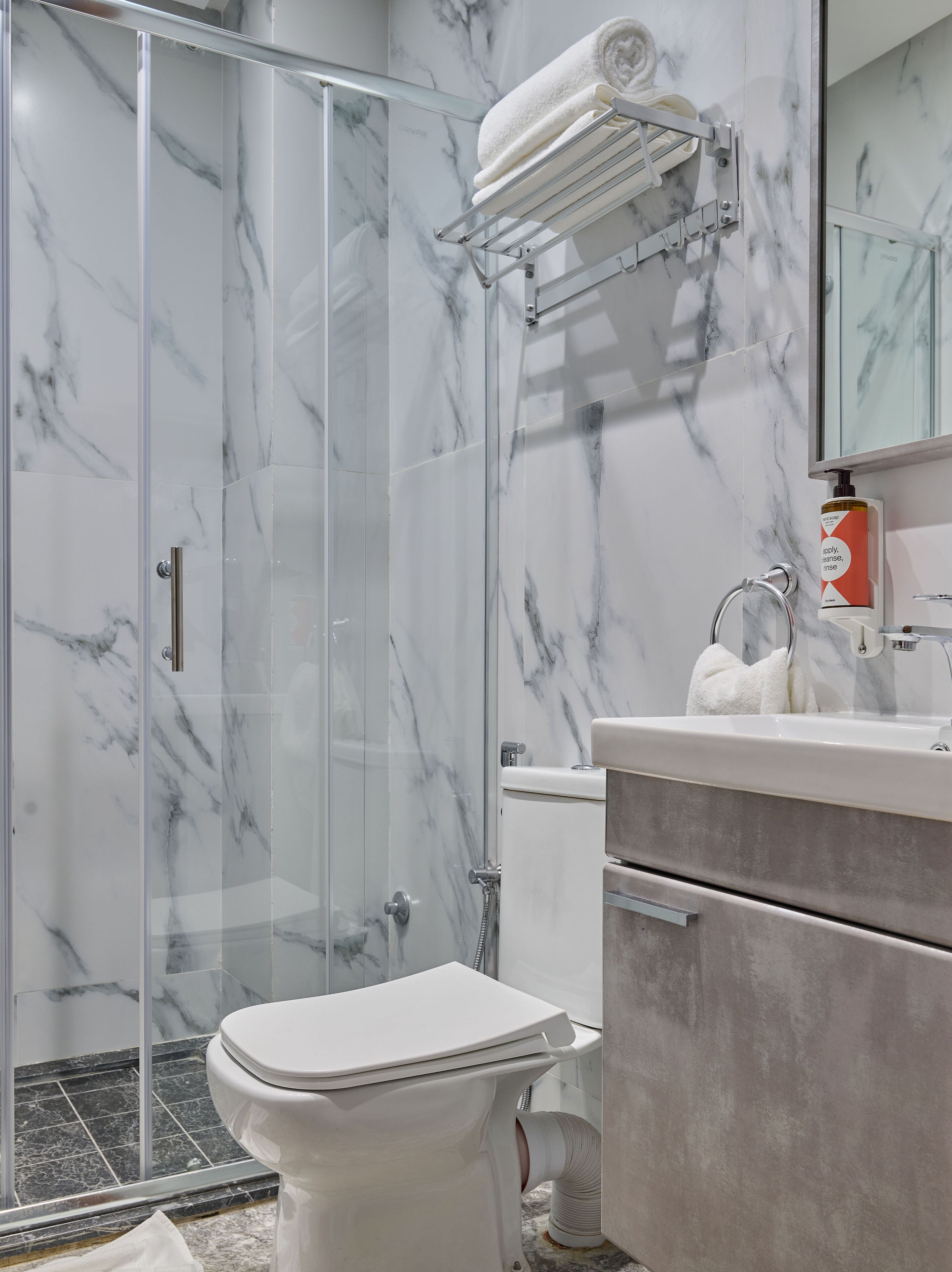Un baño moderno con cabina de ducha de vidrio, inodoro, lavamanos con encimera de mármol y un perchero para toallas.