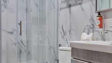 Un baño moderno con cabina de ducha de vidrio, inodoro, lavamanos con encimera de mármol y un perchero para toallas.
