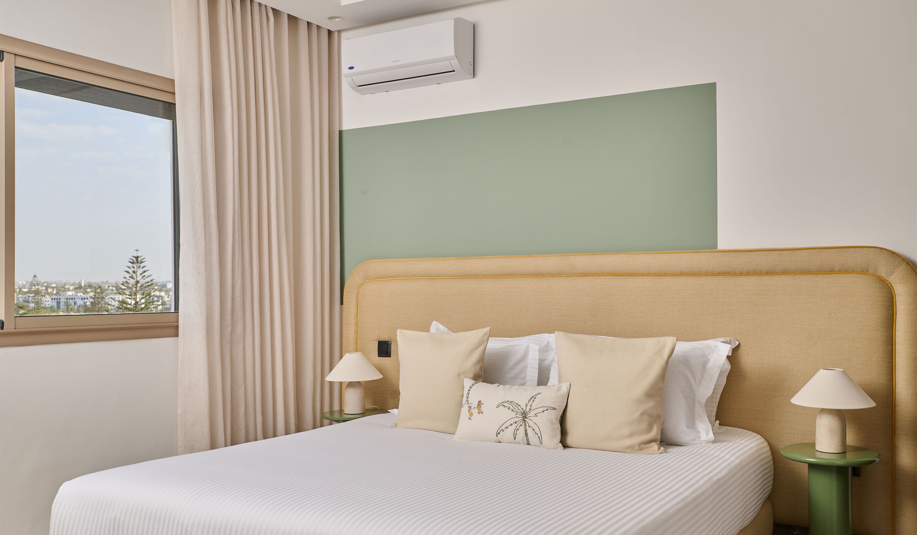 Habitación de hotel con cama, dos lámparas de noche, una ventana con cortinas y un equipo de aire acondicionado.