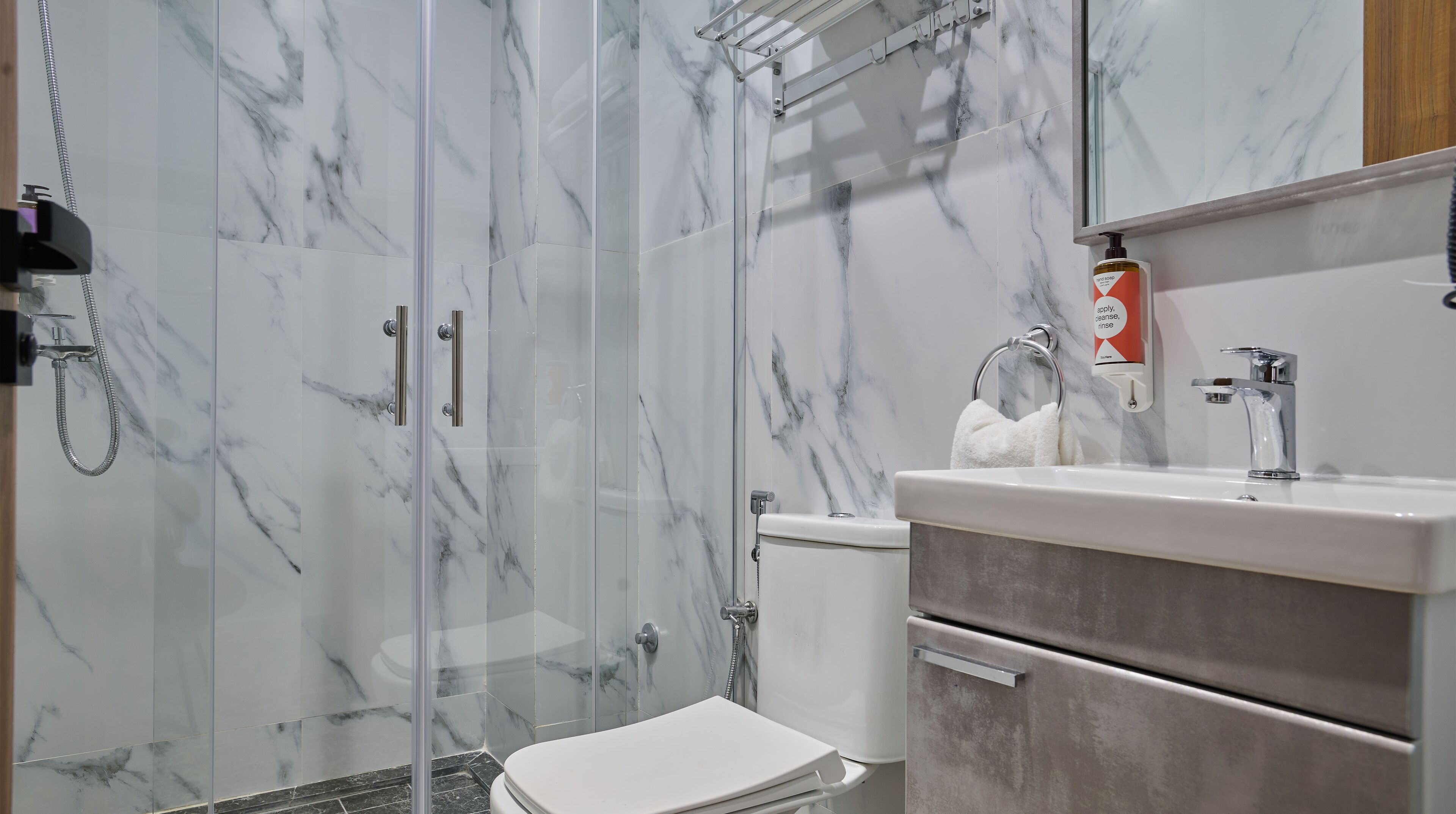 Une salle de bain avec une douche à parois de verre, des toilettes blanches, un lavabo avec un distributeur de savon et un porte-serviettes.