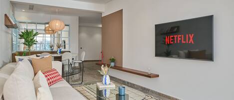 A modern living room with a sofa, coffee table, and a wall-mounted TV displaying 'NETFLIX'.