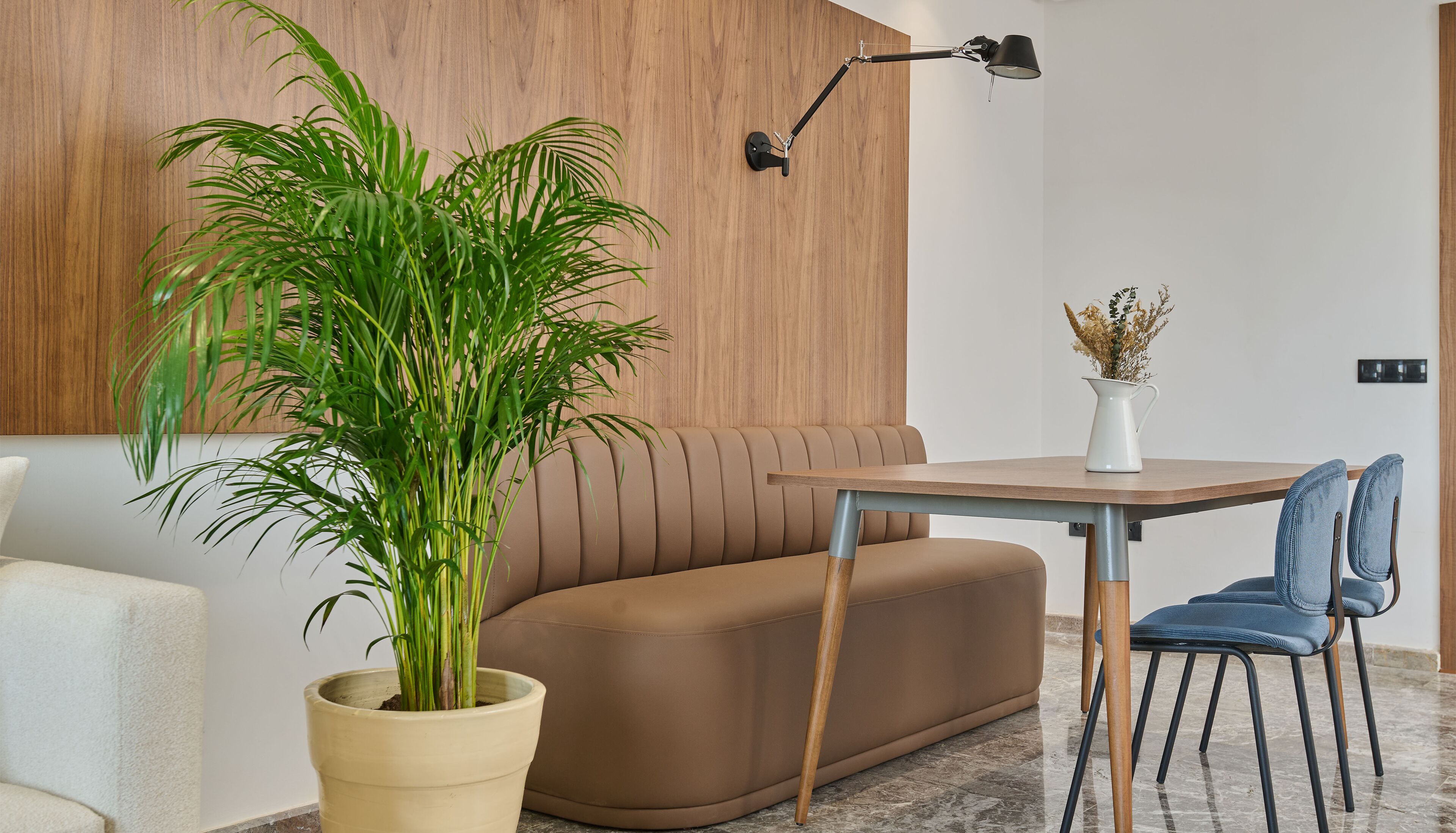 A modern living room with a brown sofa, a wooden accent wall, a potted plant, a table with a vase, and a blue chair.