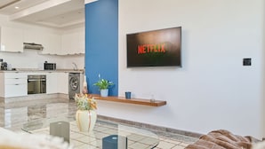 Una cocina moderna con armarios blancos, horno empotrado y lavadora. Se observa una pared de acento azul y una señal de Netflix.
