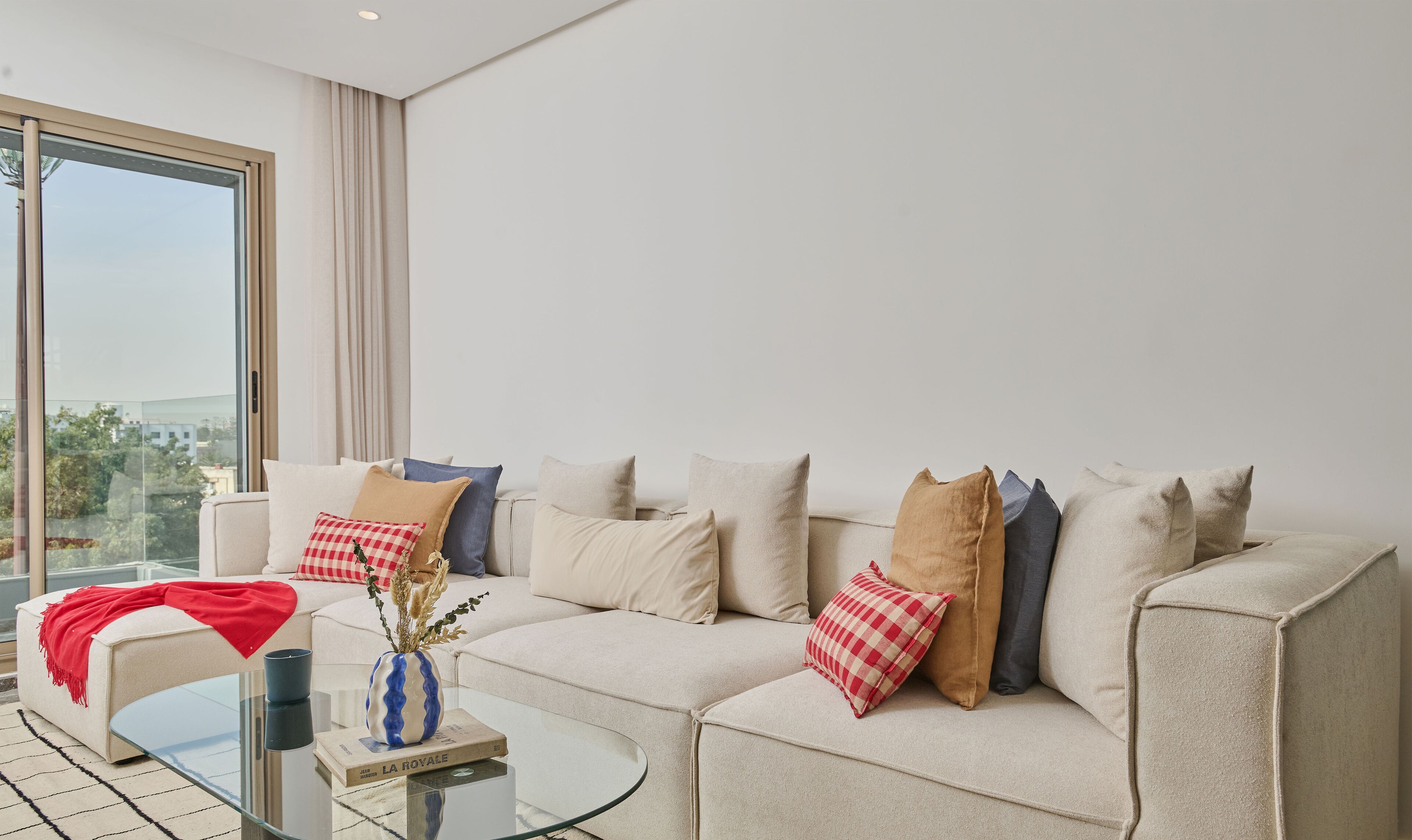 A modern living room with a sofa set, a glass coffee table, and a vase with dried plants.