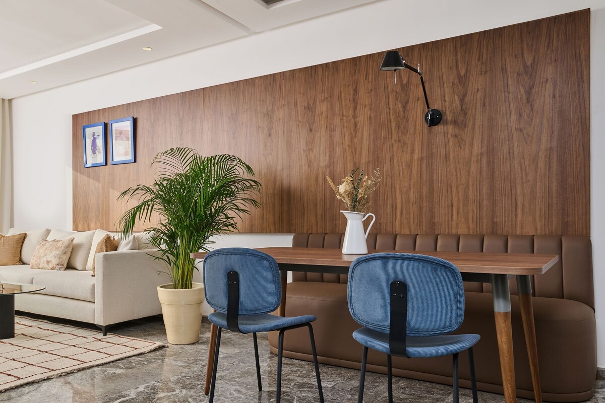 Una sala de estar moderna con un sofá, dos sillas azules, una mesita de centro, una planta y una pared de acento de madera.