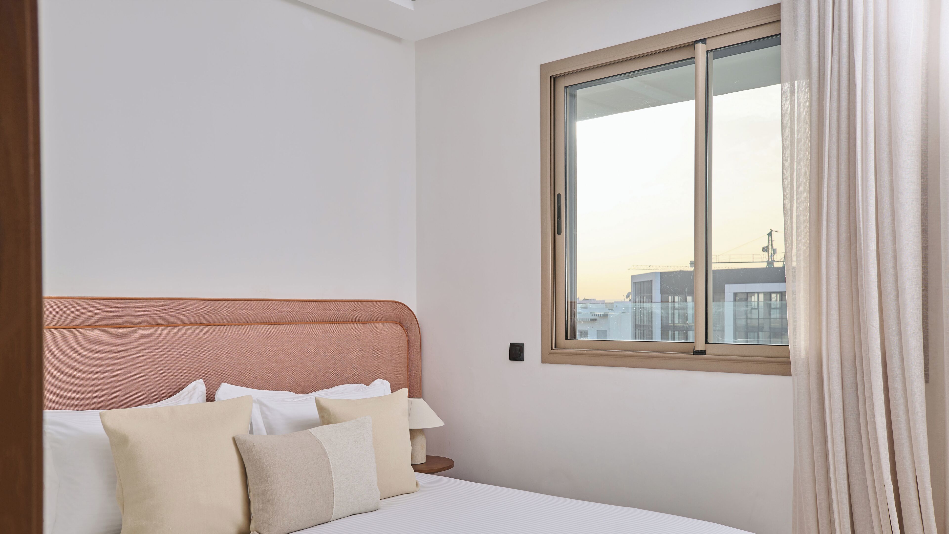 A hotel room with a bed, a window with curtains, and a view of buildings outside.