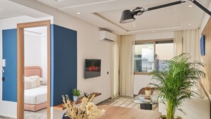 Una sala de estar moderna con una mesa de centro de vidrio, un sofá, una cama y una planta grande en maceta.