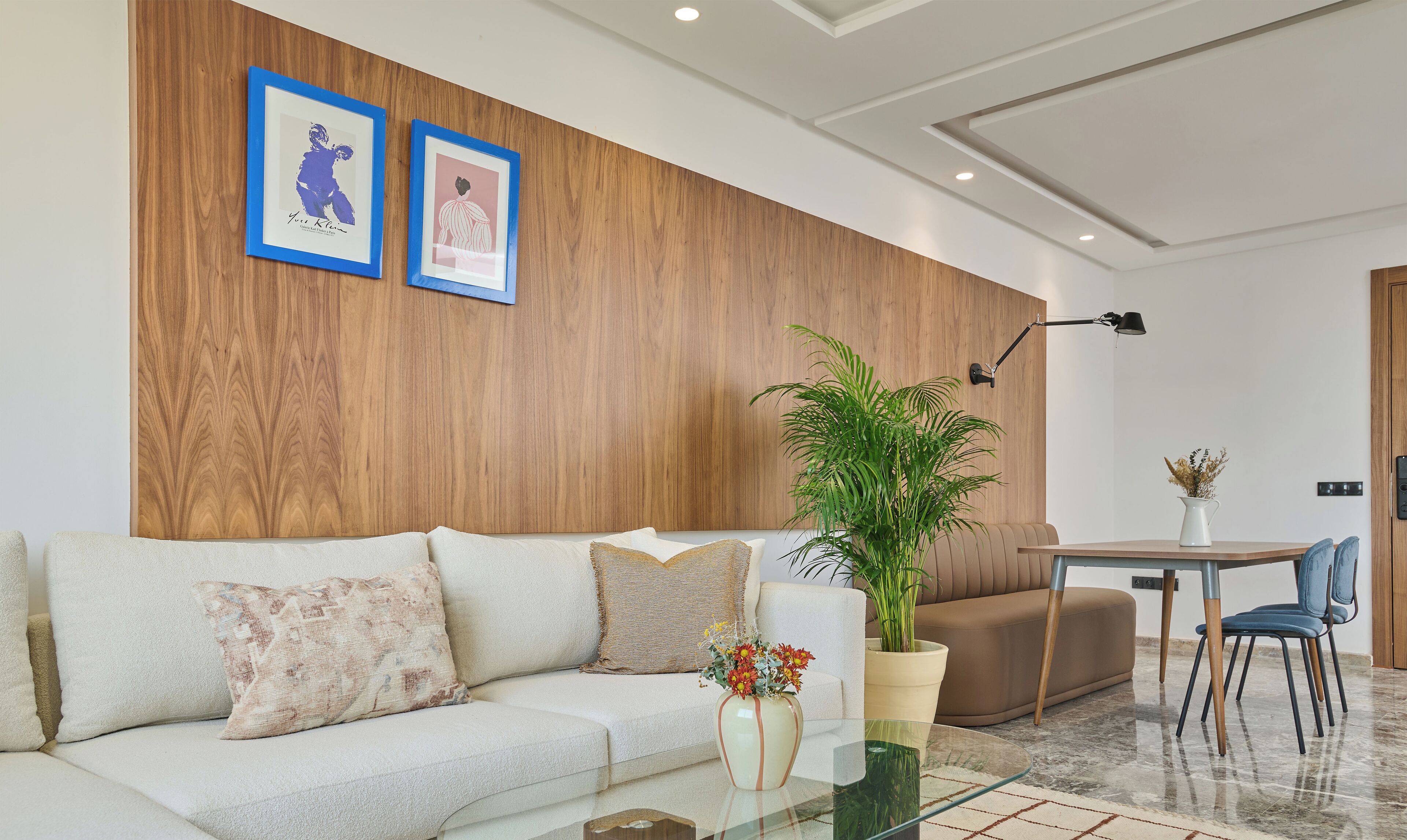 A modern living room with a wooden accent wall, a sofa, a coffee table, a potted plant, and a dining area with a chair.
