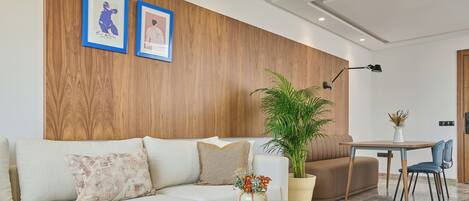A modern living room with a wooden accent wall, a sofa, a coffee table, a potted plant, and a dining area with a chair.