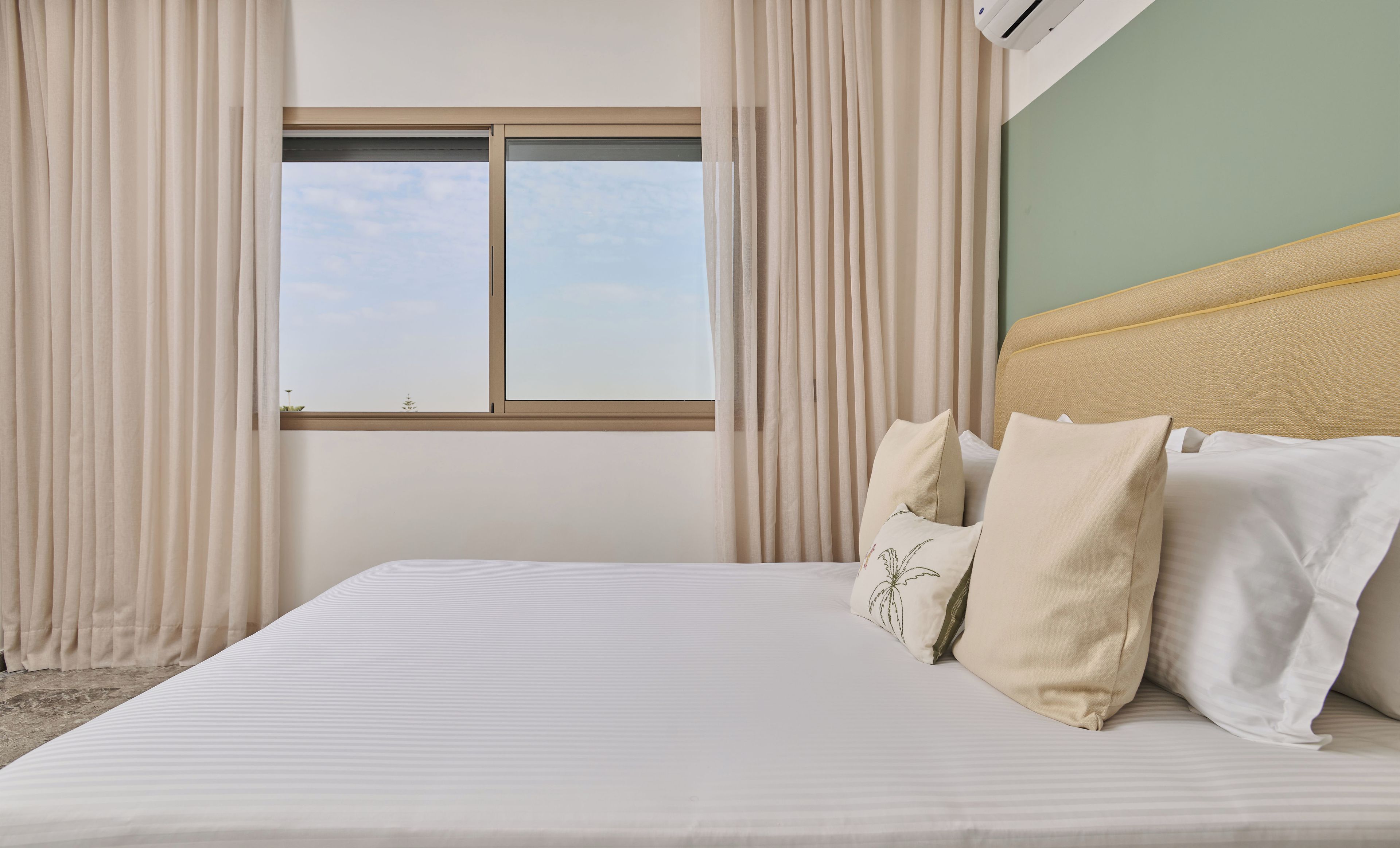 A hotel room with a large bed, beige curtains, a window with a view, and a headboard.