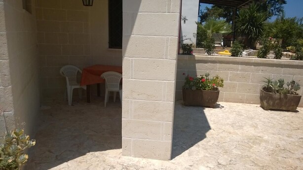 Un espace extérieur aménagé en patio, avec une table et des chaises, des plantes en pot et un mur en briques.