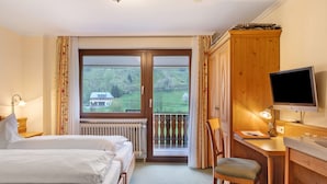 Hotellihuone, jossa on sänky, työpöytä tuolilla, televisio ja suuri ikkuna, josta avautuu näkymä vehreään maisemaan.