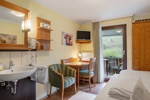 Un dormitorio con cama, escritorio con silla, televisión, baño con lavamanos y ventana.