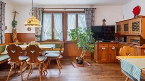 Una sala de estar acogedora con muebles de madera, una mesa de comedor, una planta en maceta y un televisor.