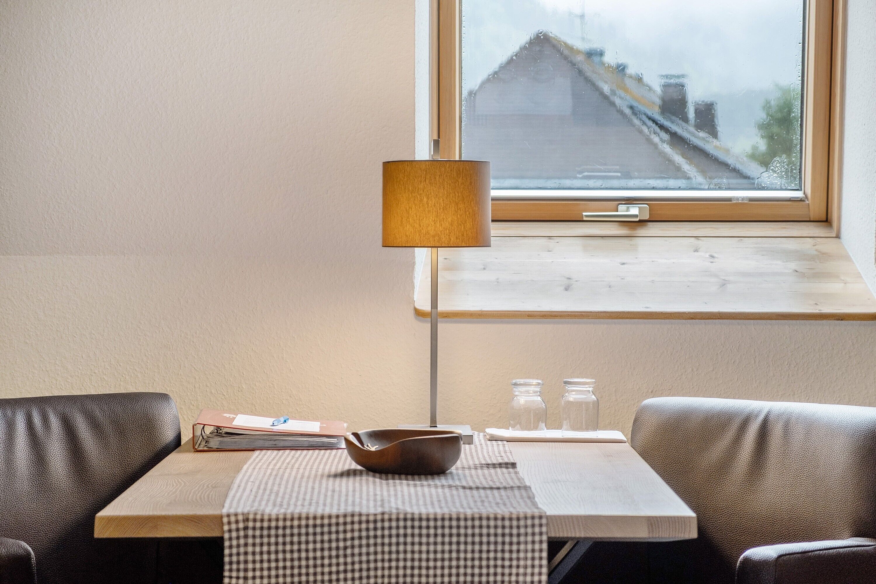 Une petite table recouverte d’une nappe à carreaux, avec un bol et des salières et poivrières. Une lampe à abat-jour carré est posée sur la table.