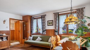 Una habitaci ón acogedora con suelo de madera, un sofá verde, una mesa de comedor de madera con sillas y una lámpara colgante.