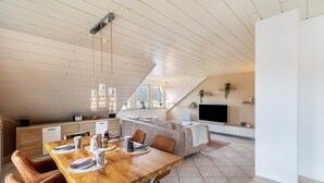 Ett modernt vardagsrum med ett matbord i trä, läderstolar, en soffa, en tv och ett köksområde.