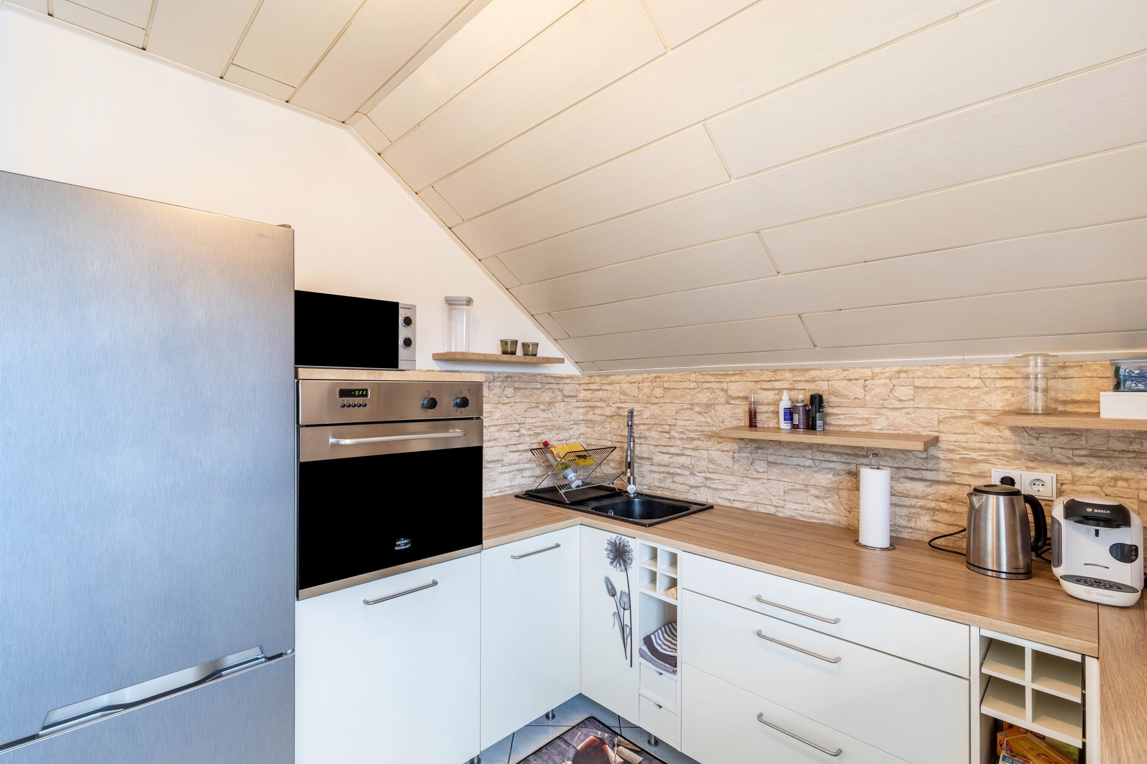 A modern kitchen with a stainless steel refrigerator, double oven, and a sink with a stone backsplash.