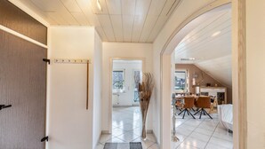 En hall som leder till en matplats med ett klinkergolv, en vas med grenar och utsikt över omgivningen.