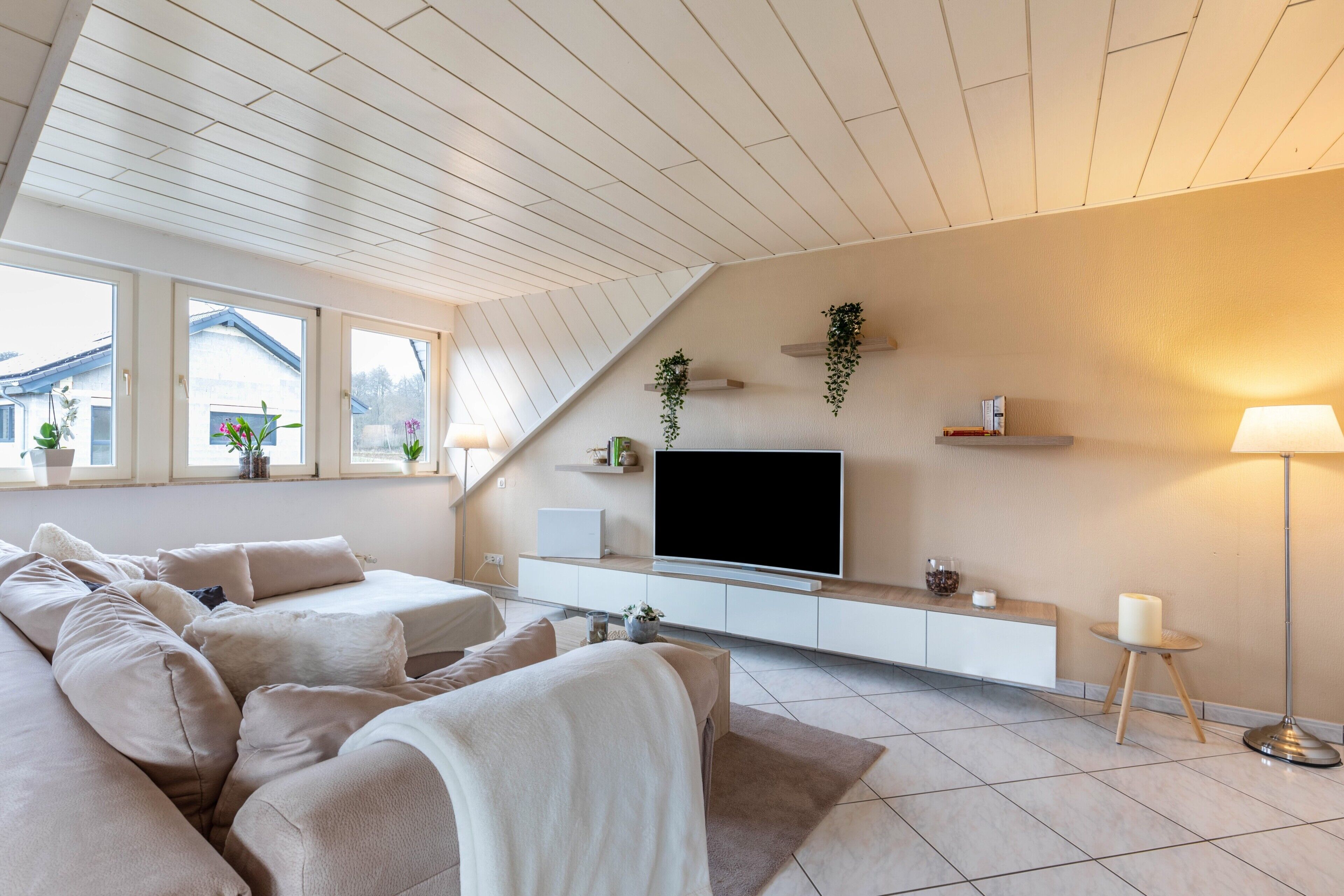 Un salon moderne doté d’un grand canapé, d’un téléviseur à écran plat et d’un plafond avec des poutres en bois.