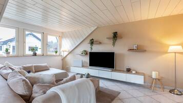 Un salon moderne doté d’un grand canapé, d’un téléviseur à écran plat et d’un plafond avec des poutres en bois.