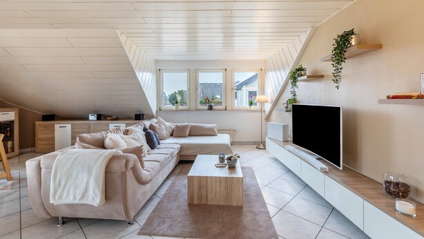 Ett modernt vardagsrum i loftstil med en soffa, ett soffbord, en tv och ett köksområde med diskmaskin.