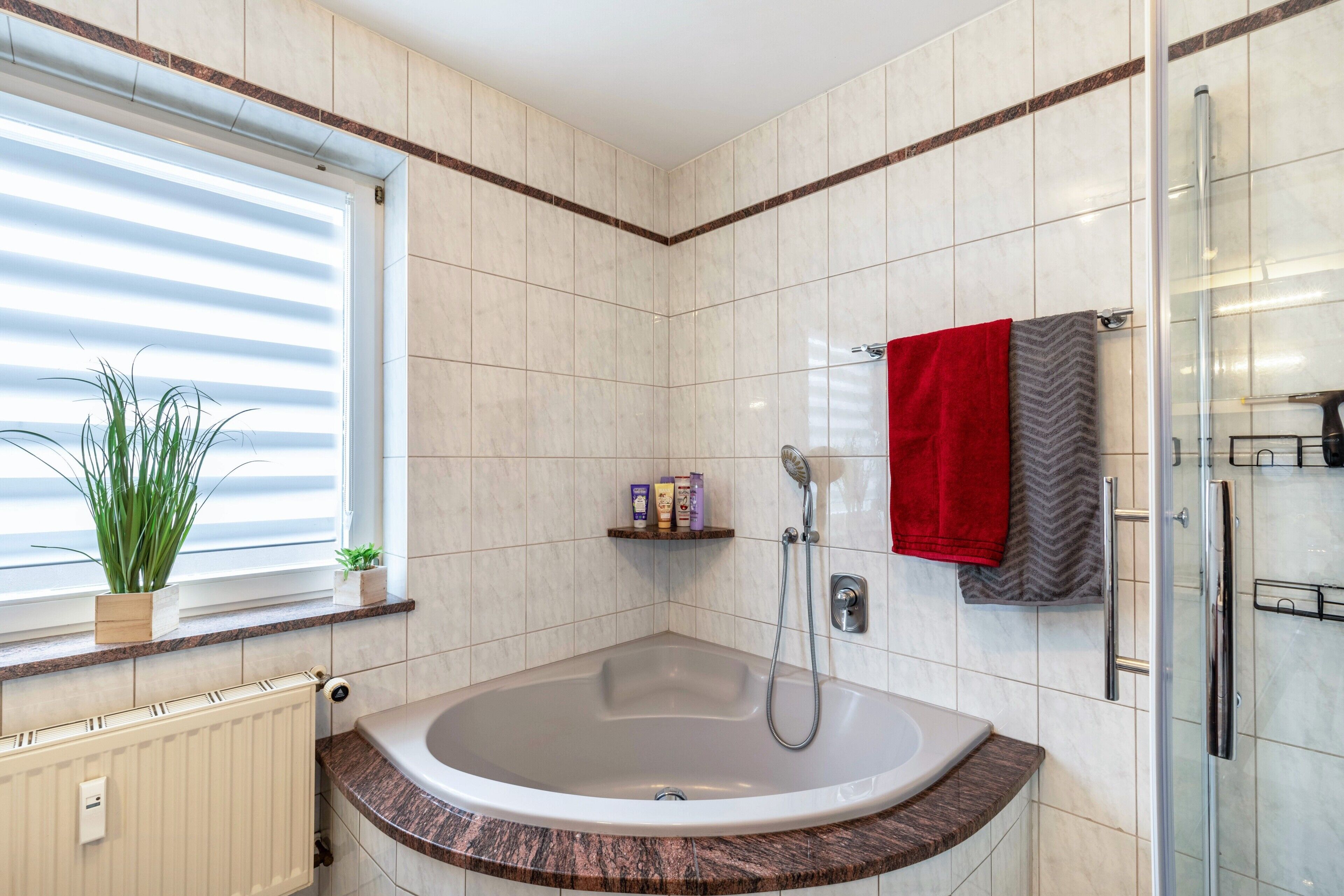 A modern bathroom with a freestanding bathtub, a glass shower enclosure, and a window with blinds.