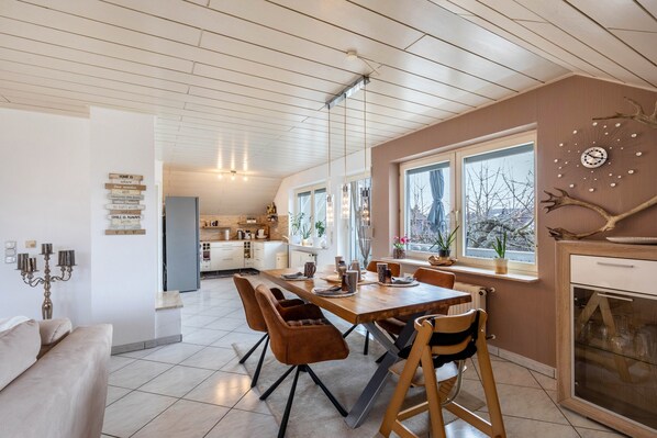 A modern kitchen with a dining area, wooden ceiling, and large windows.