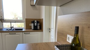 A kitchen with white cabinets, a coffee maker, a bottle of wine, and a window with a view of greenery. - Apartment 'Repetal' with Private Terrace, Garden and Wi-Fi (Attendorn)
