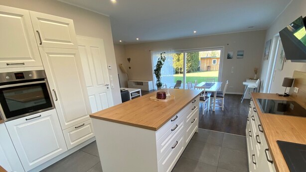 A modern kitchen with white cabinetry, a wooden island, and a dining area with a view of the outdoors. - Apartment 'Repetal' with Private Terrace, Garden and Wi-Fi (Attendorn)