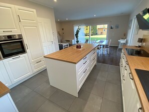 A modern kitchen with white cabinetry, a wooden island, and a dining area with a view of the outdoors.