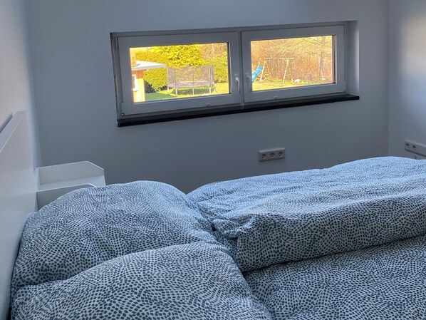 A bedroom with a bed, a window, and a wall-mounted shelf.