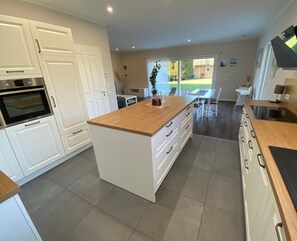 Una cocina moderna con armarios blancos, una isla de madera y un comedor con mesa y sillas.