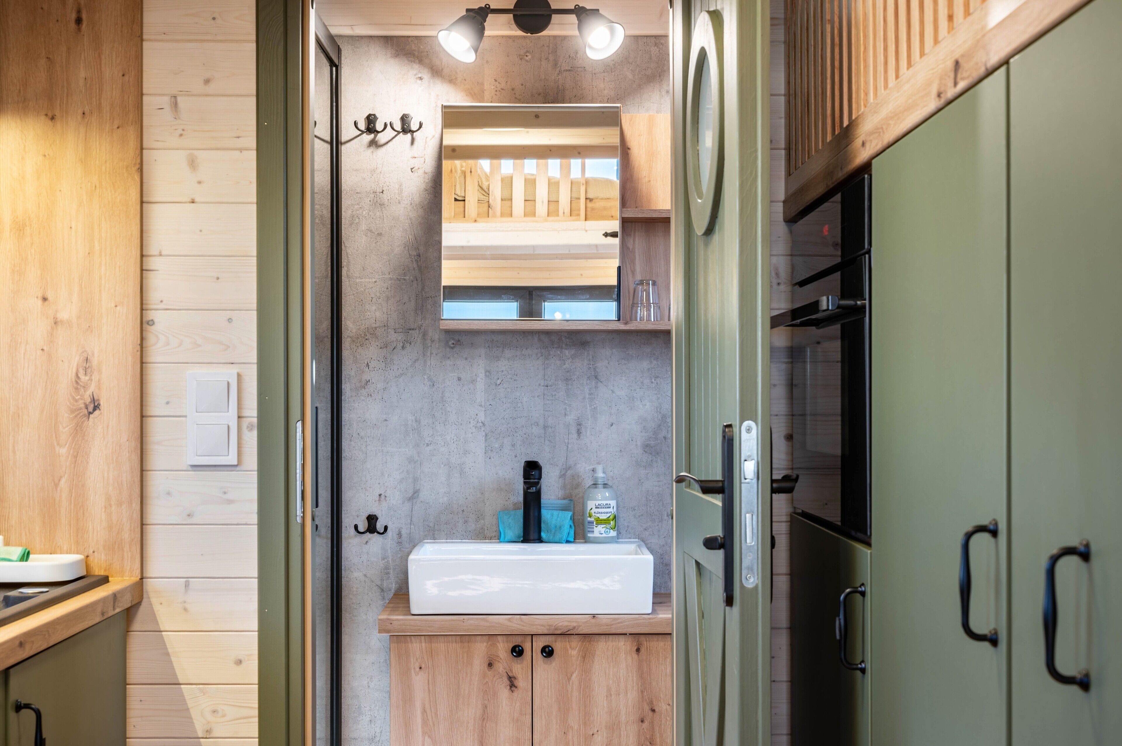 A compact kitchen with a wooden countertop, a white sink, and a wooden shelf above.