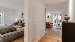 A modern bedroom with a bed, a white door, and a view to a living area with a sofa and a table. - Exclusive holiday flat - just a few steps from the lake (Überlingen)