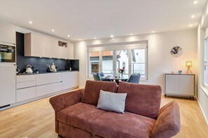 A modern living area with a sofa, a dining table with chairs, a kitchen with cabinets, and a window with a view.