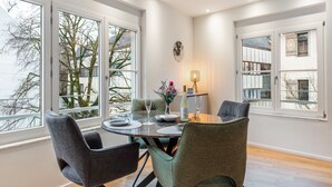 A dining area with a round table, four chairs, a vase with flowers, a bottle of wine, and a wall-mounted fan. - Exclusive holiday flat - just a few steps from the lake (Überlingen)