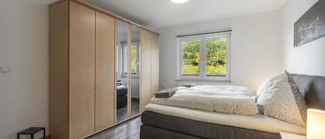 A bedroom with a bed, a wardrobe, a window with a view, and a bedside table with a lamp.