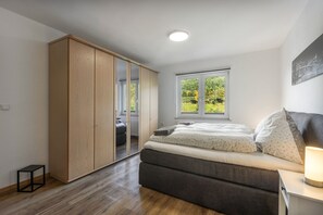 A bedroom with a bed, a wardrobe, a window with a view, and a bedside table with a lamp.
