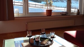A room with a view of a snowy landscape, a table with candles, and a potted plant on the windowsill. - Apartment 'Rasche' with Balcony (Schmallenberg)
