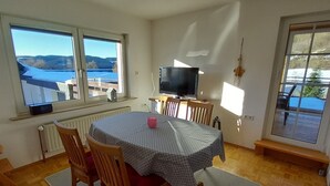 A dining area with a table, chairs, a television, and a view of a snowy landscape through large windows. - Apartment 'Rasche' with Balcony (Schmallenberg)