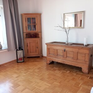 Une pièce comprenant un meuble en bois, un miroir, un vase avec des branches et un lampadaire.