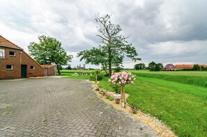 Ein gepflasterter Weg führt zu einem Backsteinhaus mit grüner Tür, umgeben von einer grünen Wiese und einem Baum mit rosa Blüten.