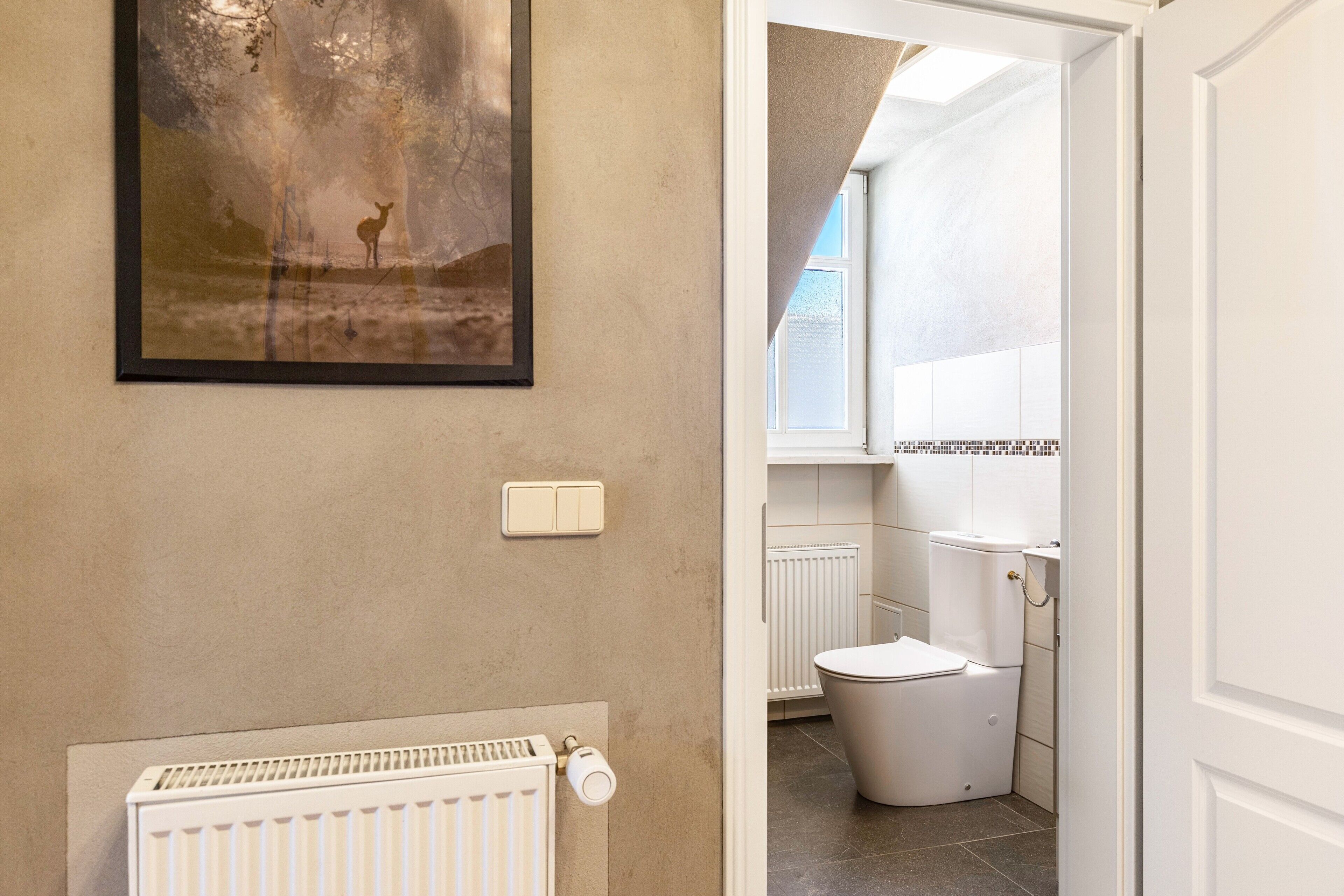 Ein Badezimmer mit Toilette, Heizkörper und einem gerahmten Bild an der Wand.