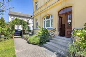 A building with a yellow facade, a wooden door, and a brick pathway leading to a set of stairs. - Apartment 'Quartier' with Wi-Fi (Bad Freienwalde (Oder))