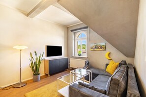 A modern living room with a sofa, a coffee table, a floor lamp, a TV, and a window with a view. - Apartment 'Quartier' with Wi-Fi (Bad Freienwalde (Oder))
