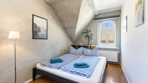Un dormitorio con una cama, una lámpara, un cuadro enmarcado, una ventana y una planta.