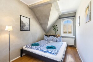 Une chambre à coucher avec un lit, une lampe, un tableau encadré, une fenêtre et une plante.