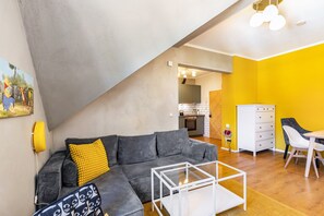 A modern living room with a grey sectional sofa, a glass coffee table, and a dining area with a white table and chairs.