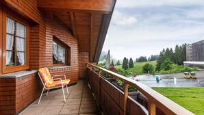 A wooden balcony with a chair, a view of a road, and a building in the background. - Holiday Apartment 'Type B, 50sqm' with Mountain View, Private Terrace and Wi-Fi (Feldberg (Schwarzwald))